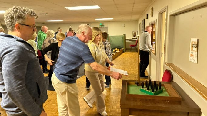 A group of people playing a game involving wooden pins indoors.