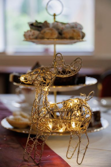 A decorative gold reindeer with fairy lights in front of a tiered cake stand with sweets.